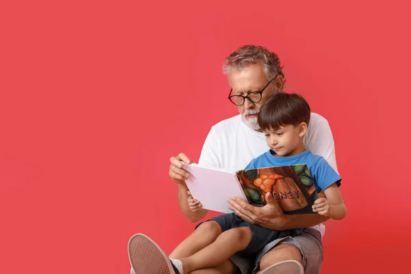 Senior Man Läser Bok För Sin Lilla Sonson Röd Bakgrund — Stockfoto