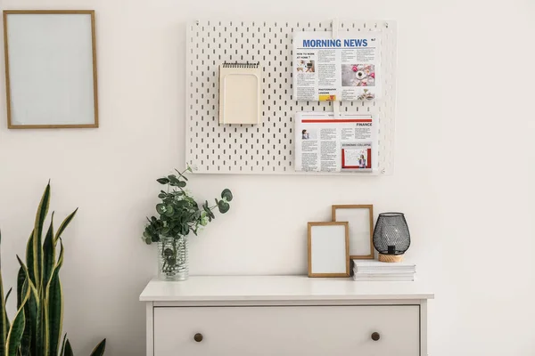 Pegboard with notebooks and newspapers hanging on light wall in room