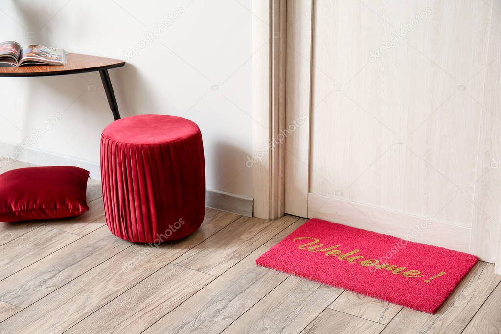 Stylish pouf and mat near wooden door in hall