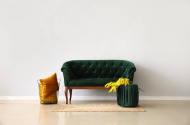 Yeşil kanepe, çiçekli puf ve ışık duvarının yanında sepet.