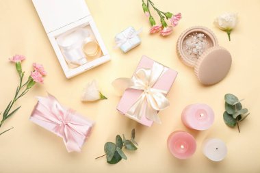 Sarı arka planda çiçekler, mumlar ve hediye kutularıyla güzel bir kompozisyon.