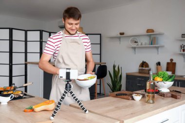 Genç adam mutfakta video çekerken salata yapıyor.