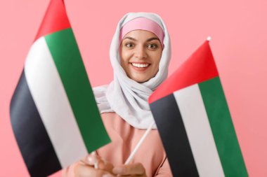 Geleneksel giyinmiş genç bir kadın ve arka planında BAE 'nin ulusal bayrakları var.