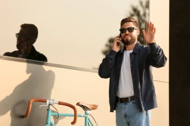 Bisikletli şık sakallı adam şehirde cep telefonuyla konuşuyor.