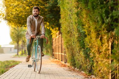 Genç sakallı iş adamı bisiklet sürüyor.