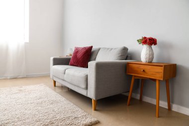 Ahşap komodinli şık bir iç mekan ve açık gri duvarın yanındaki kanepe.