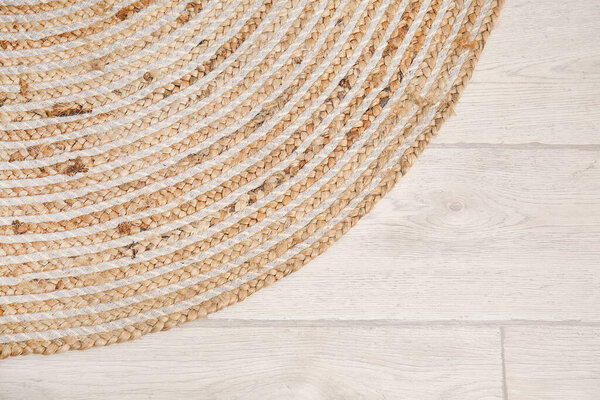 Stylish wicker rug on light wooden floor, closeup