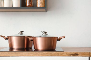 Mutfaktaki ışık duvarının yanındaki ocakta parlak tencereler.