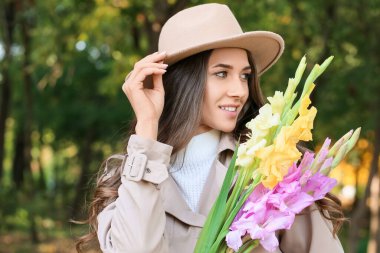 Şık keçeli şapka takan ve parkta elinde bir buket Gladiolus çiçeği tutan bir kadın.