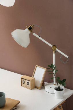 Beyaz lamba, çerçeve, takvim ve saksı kahverengi duvarın yanında.