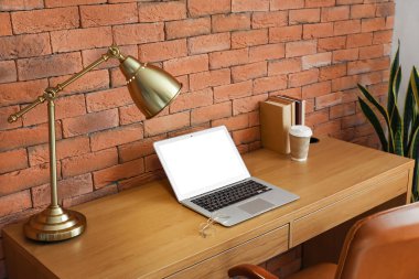 Dizüstü bilgisayarı ve tuğla duvarın yanında altın lambası olan modern işyeri