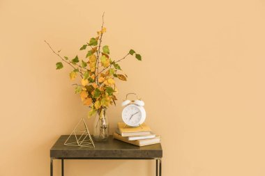 Sonbahar dallı vazo, renkli duvarın yanındaki masada yığınla kitap ve çalar saat.