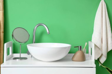 Yeşil duvarın yanında beyaz lavabolu, aynalı ve sabunlu bir masa.