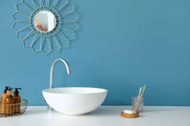 Mavi duvarın yanında lavabo ve banyo malzemeleri olan bir masa.