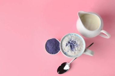 Bir fincan mavi kibrit latte, pembe arka planda toz ve süt.