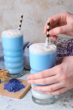 Açık arkaplanda mavi latte bardaklı kadın elleri, yakın plan.