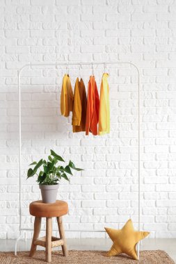 Beyaz tuğla duvarın yanındaki tabureye çocuk süveteri ve saksı dizin.