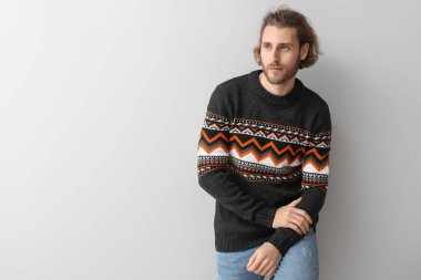 Gri arka planda örülü süveter giyen yakışıklı genç adam.