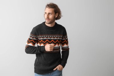 Gri arka planda örülü süveter giyen yakışıklı genç adam.