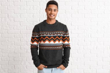 Beyaz tuğla arka planda örgü kazak giyen yakışıklı Afro-Amerikalı adam.