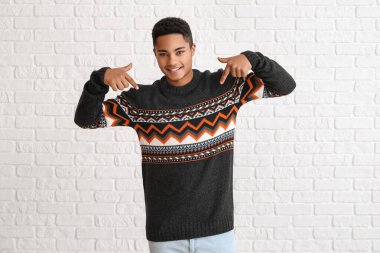 Beyaz tuğla arka planda örgü kazak giyen yakışıklı Afro-Amerikalı adam.