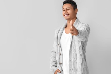 Örgü süveter giyen yakışıklı Afro-Amerikalı arka planda baş parmağını kaldırıyor.