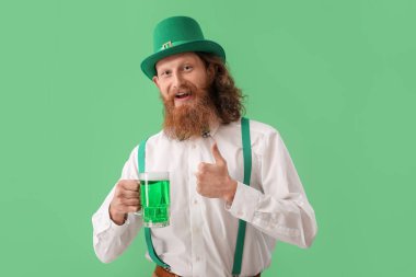 Bir bardak birası olan mutlu sakallı adam yeşil arka planda baş parmağını kaldırıyor. Aziz Patrick Günü kutlaması