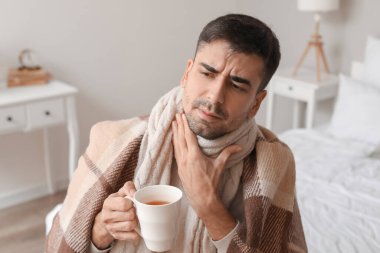 Boğazı ağrıyan, evde sıcak çay içen genç bir adam.