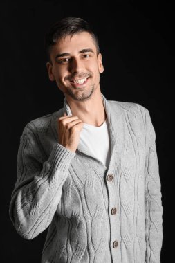 Esmer arka planda örülü süveter giyen yakışıklı bir genç.