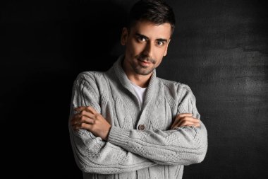 Esmer arka planda örülü süveter giyen yakışıklı bir genç.
