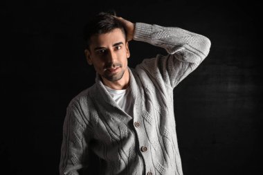 Esmer arka planda örülü süveter giyen yakışıklı bir genç.