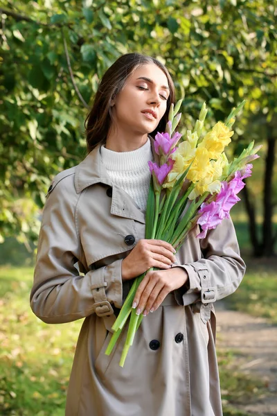 若いです目を閉じた女性保持花束のグラジオラス花で公園 — ストック写真