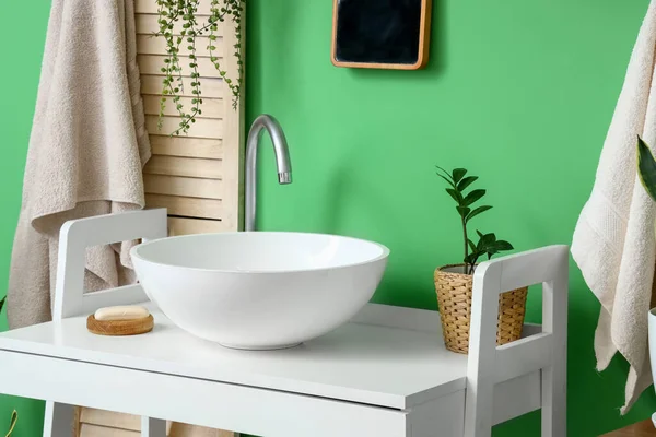 Beyaz lavabolu masa, yeşil duvarın yanında bitki ve sabun.