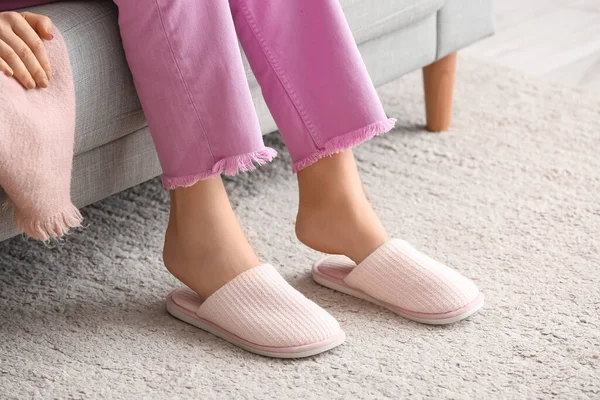 Evdeki kanepede oturan yumuşak terlikli genç kadın.