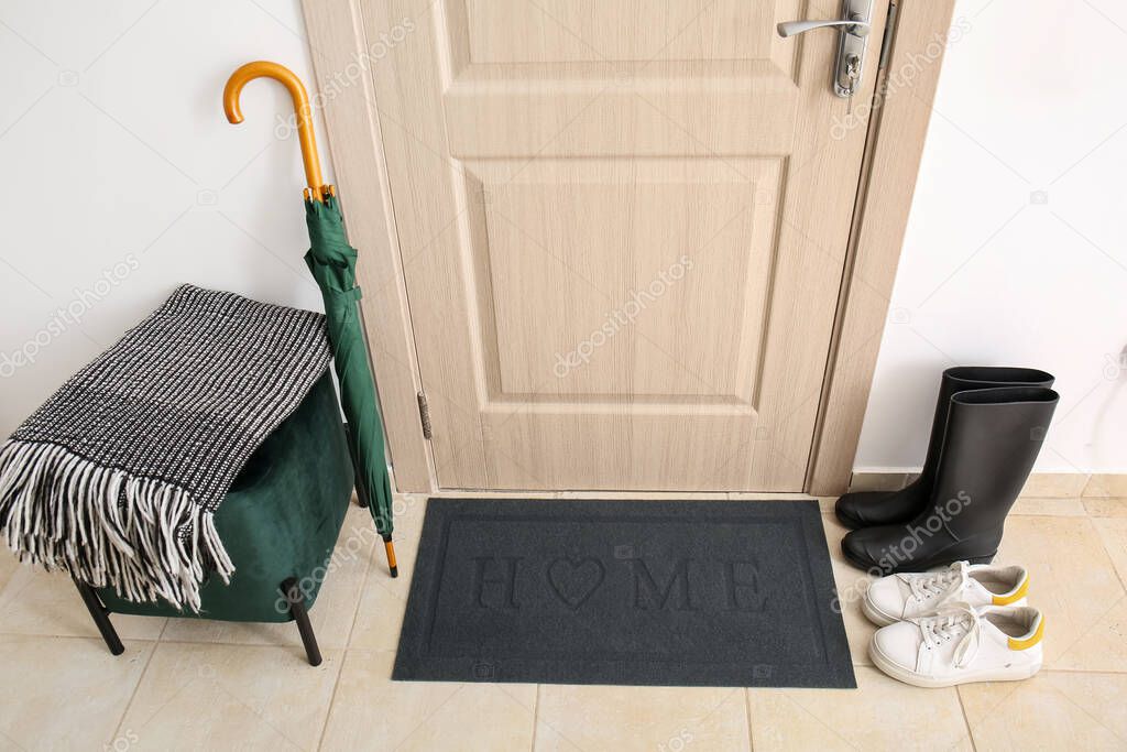 Black mat with shoes, umbrella and pouf near light wooden door