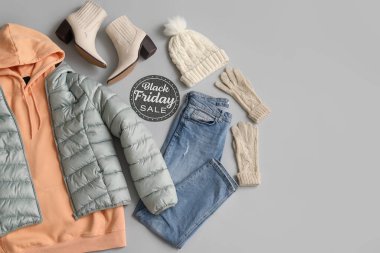 Siyah Cuma satışı yazılı kağıt, kalın kadın giysileri, aksesuarlar ve gri arka planda ayakkabılar