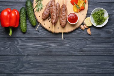 Lezzetli lula kebabı, sos ve sebzeli şiş tahtası siyah ahşap arka planda.