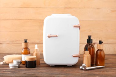 Küçük buzdolabı ve kozmetik ürünleri ahşap masada.