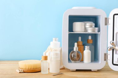 Ahşap masada kozmetik ürünleri olan küçük bir buzdolabı.