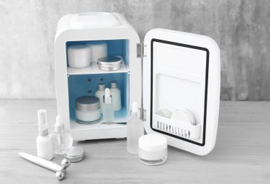 Hafif ahşap masada kozmetik ürünleri olan küçük bir buzdolabı.