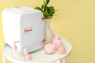 Renk duvarının yanındaki masada küçük buzdolabı ve kozmetik ürünleri