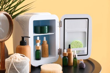 Renk duvarının yanındaki masada kozmetik ürünleri olan küçük bir buzdolabı.