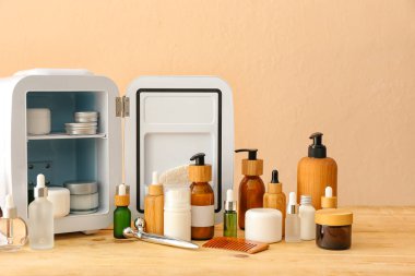 Ahşap masada kozmetik ürünleri olan küçük bir buzdolabı.