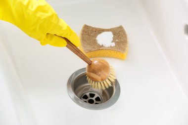 Lastik eldivenli bir kadın seramik lavaboyu fırçayla temizliyor.