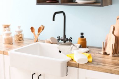 Ahşap tezgah, seramik lavabo ve mutfak malzemeleri mavi duvarın yanında.