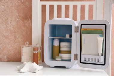 Masada ürünleri olan kozmetik buzdolabını aç ve renk duvarının yanında katlanan ekranı aç