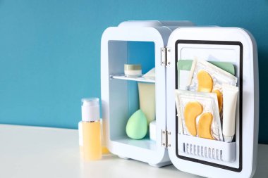 Mavi duvarın yanındaki raflarda ürünlerle birlikte kozmetik buzdolabı aç
