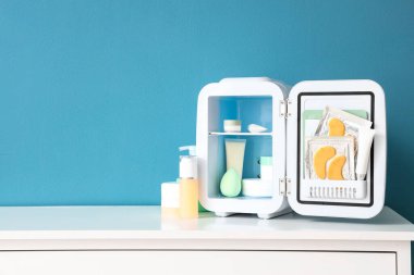 Mavi duvarın yanındaki raflarda ürünlerle birlikte kozmetik buzdolabı aç