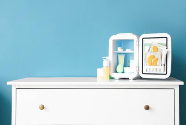 Mavi duvarın yanındaki çekmecelerin üzerindeki ürünlerle birlikte açık kozmetik buzdolabı