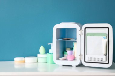 Mavi duvarın yanındaki raflarda ürünlerle birlikte kozmetik buzdolabı aç